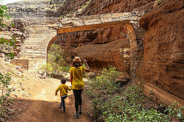 A woman and a child are walking through a rocky area. The woman is wearing a yellow shirt and a hat