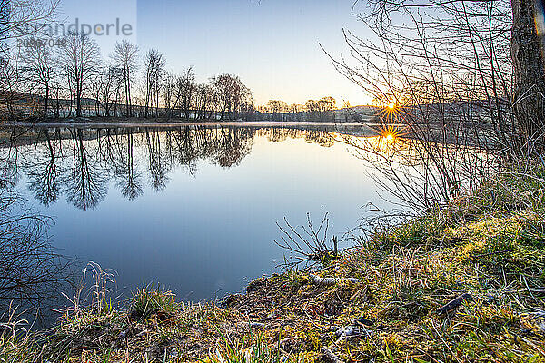 View from the shore into the distance and a sunset on the lake. The surroundings and the marvellous sky are reflected in the water. A great landscape shot Dutenhofener See  Hesse Germany