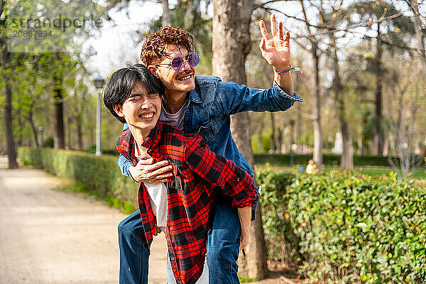 Horizontal photo with copy space of a gay couple having fun in a park waving and piggybacking