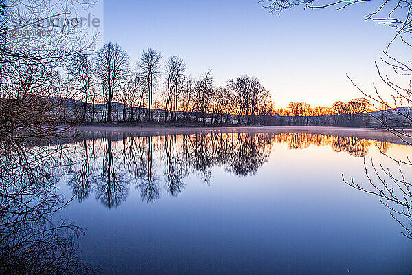 View from the shore into the distance and a sunset on the lake. The surroundings and the marvellous sky are reflected in the water. A great landscape shot Dutenhofener See  Hesse Germany