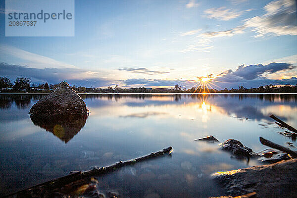 View from the shore into the distance and a sunset on the lake. The surroundings and the marvellous sky are reflected in the water. A great landscape shot Dutenhofener See  Hesse Germany