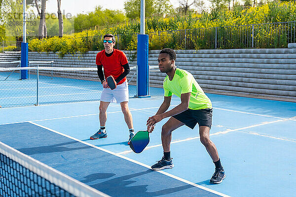 Full length photo of a multiracial team of pickleball players in an outdoor court in a sunny day