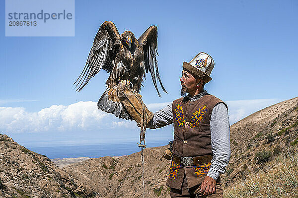 Traditional Kyrgyz eagle hunter with eagle in the mountains  hunting  eagle spreads its wings  near Bokonbayevo  Issyk Kul region  Kyrgyzstan  Asia