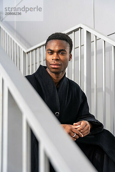 Vertical portrait of a handsome african american model with black warm clothes sitting on outdoor stairs