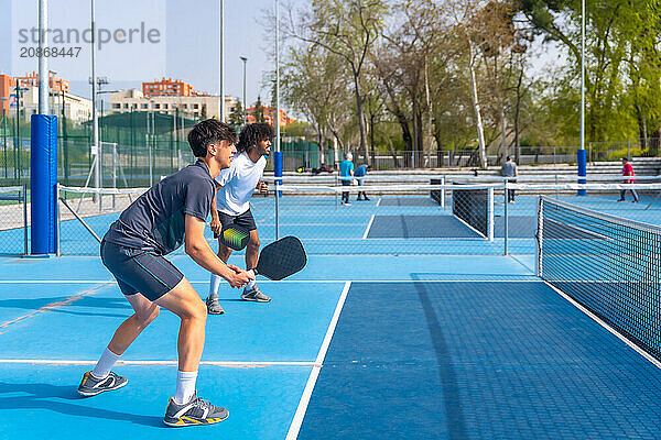 Full length side view of a multi-ethnic pickleball team playing with friends in an outdoor court