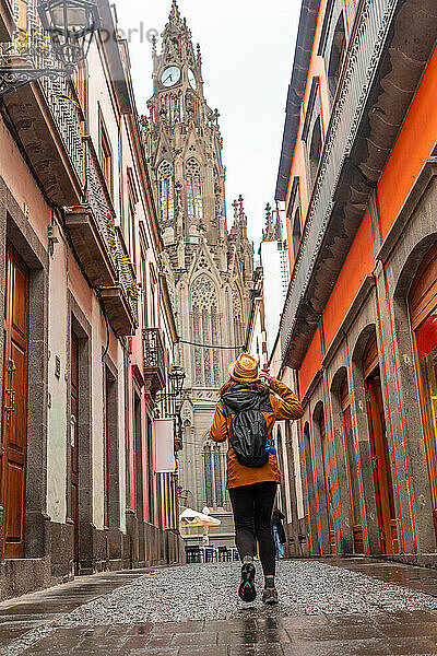 A tourist woman with a hat walking along a beautiful street next to the Church of San Juan Bautista  Arucas Cathedral  Gran Canaria  Spain  Europe