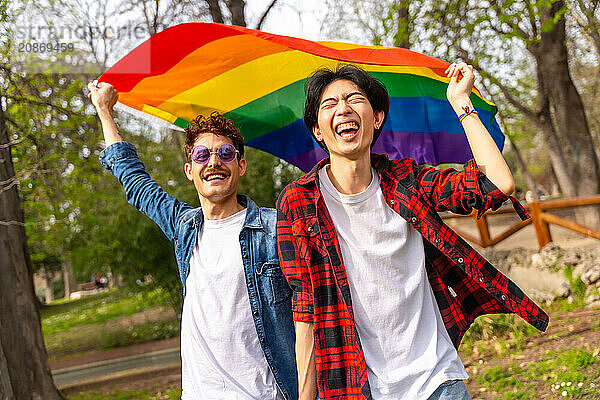 Portrait of happy multi-ethnic gay people waving lgbt rainbow flag in a park