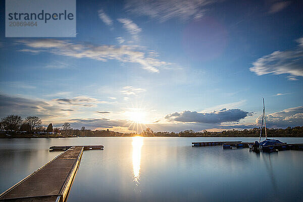 View from the shore into the distance and a sunset on the lake. The surroundings and the marvellous sky are reflected in the water. A great landscape shot Dutenhofener See  Hesse Germany