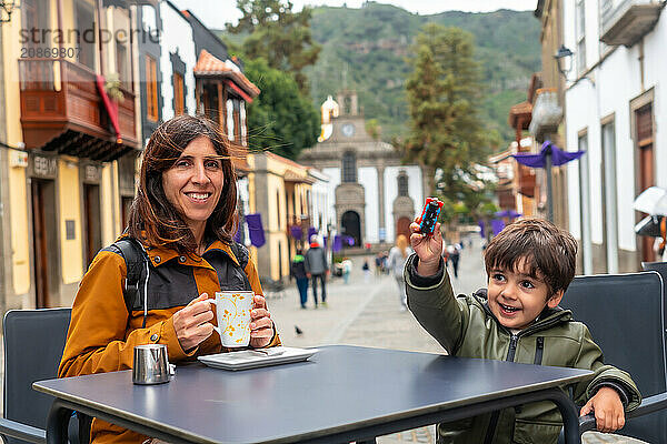 A woman and a child are sitting at a table in a city street  smiling and enjoying their time together