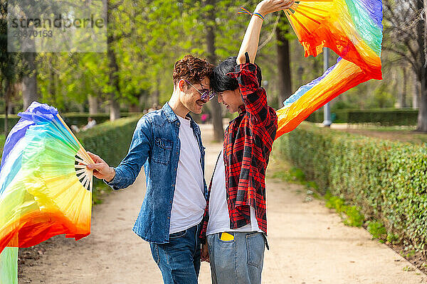 Side view of a multi-ethnic gay couple dancing using rainbow fans