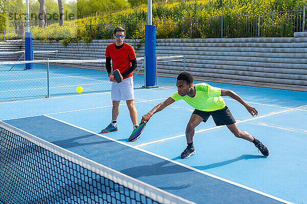 African man trying to reach the ball playing pickleball with a caucasian male partner in an outdoor court