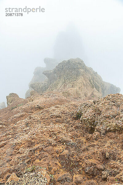 A rocky hillside with a foggy sky in the background. The fog is thick and the rocks are jagged and rough. The scene is desolate and eerie  with the fog adding to the sense of mystery and isolation