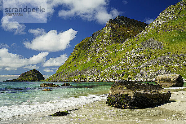 Landscape with sea at the sandy beach of Haukland (Hauklandstranda) with the mountain Veggen. Some rocks on the beach and in the sea. Blue sky  some clouds. Early summer. Haukland Beach  Haukland  Vestvagoya  Lofoten  Norway  Europe