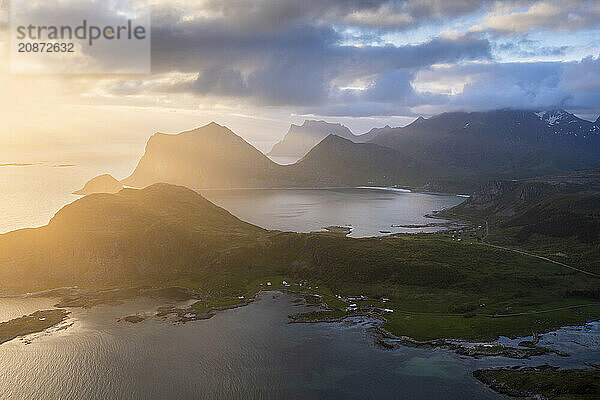 Landscape on the Lofoten Islands. View from the mountain Offersoykammen to the sea  the mountains Veggen  Mannen  Himmeltindan and Hogskolmen as well as the beaches of Haukland (Hauklandstranda) and Vik (Vik Beach) . At night at the time of the midnight sun. Clouds in the sky  sunlight from the side. Vestvagoya  Lofoten  Norway  Europe