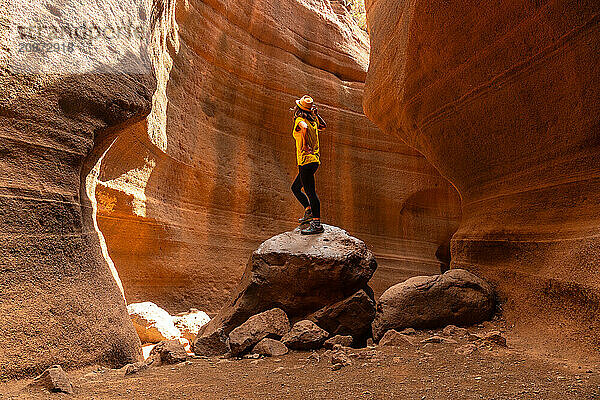 A person is standing on a rock in a canyon. The canyon is filled with rocks and dirt  and the person is wearing a yellow shirt