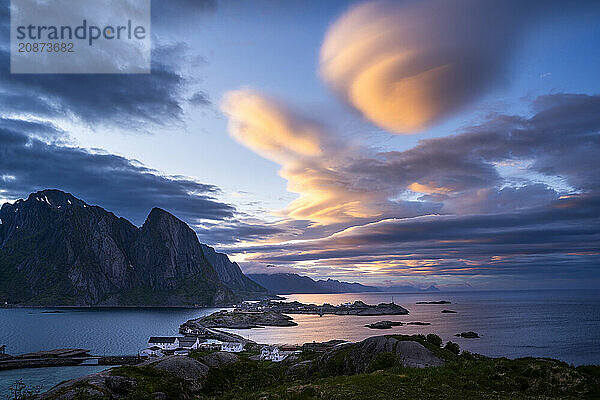 Cloudy landscape. The villages of Olenilsoy  Toppoya (Toppoy) and Hamnoy as well as the Festhaeltinden mountain. A bridge connects the islands. View across the sea towards Flakstadoya and Vestvagoya. Several coloured lenticular clouds (lenticularis) in the blue sky. At night at the time of the midnight sun. Early summer. Moskenesoya  Lofoten  Norway  Europe