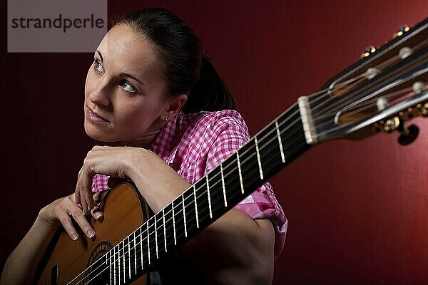 Woman holding classical guitar in front of red background