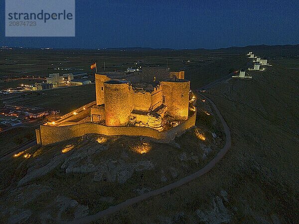 An illuminated castle at night with a dark sky and a path surrounding the castle  aerial view  windmills in the background  Consuegra  Toledo  Castilla-La Mancha  Spain  Europe