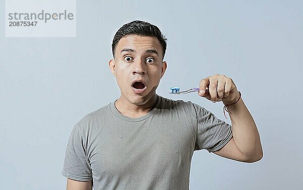 Amazed young man holding toothbrush with toothpaste isolated  guy with wow expression holding toothbrush isolated on white  Surprised young man holding a toothbrush with toothpaste