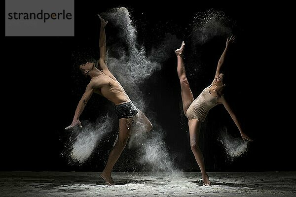 Young man and woman posing emotionally face to face to each other with their hands up and streching gracefully in cloud of white dust studio shot