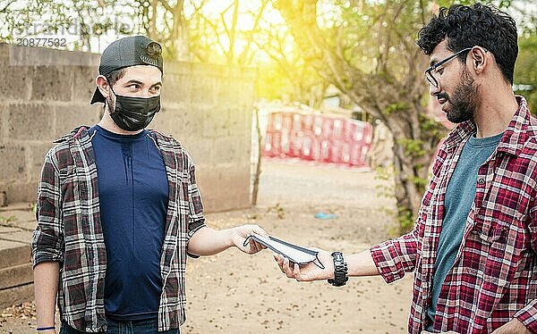 Side view of young man giving a surgical mask to another person  concept of a person giving a surgical mask  Two young people giving each other a surgical mask