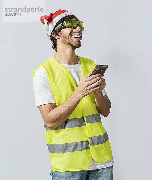 Happy Engineer in christmas hat using cell phone isolated. Smiling engineer in christmas hat using cell phone. Concept of engineer with christmas hat laughing while using cell phone at christmas