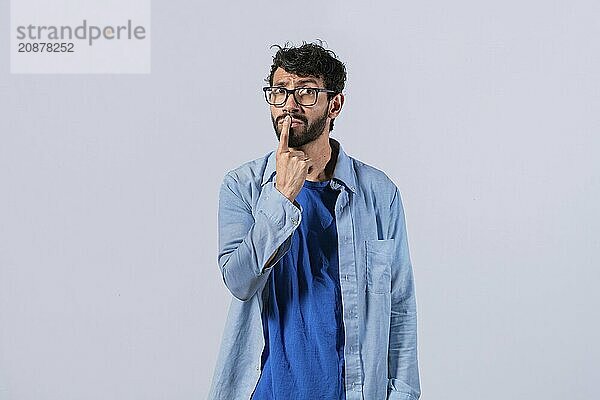 Pensive young man with finger on his lips on an isolated background. Worried guy with finger on his lips thinking isolated