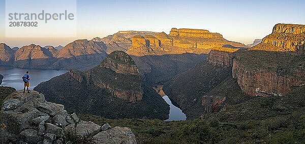 Tourist enjoying the view from a rock  Panorama  Sunset at Blyde River Canyon with Three Rondawels peak  View of canyon with Blyde River and Table Mountains in the evening light  Canyon landscape  Panorama Route  Mpumalanga  South Africa  Africa