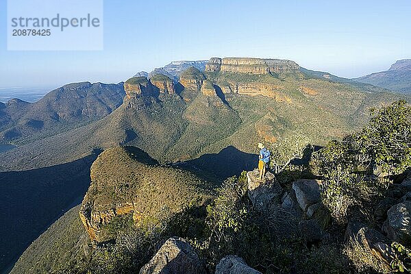 Tourist standing on a rock and enjoying the view of the canyon  Blyde River Canyon with Three Rondawels peak  View of canyon with Blyde River and Table Mountains  Canyon landscape in the evening light  Three Rondavels Viewpoint  Panorama Route  Mpumalanga  South Africa  Africa