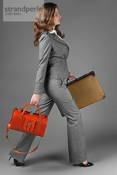 A businesswoman with a bag and a suitcase. On a gray background