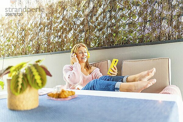 Caucasian adult woman lying on the patio listening to music with mobile phone and headphones under the shadow of an umbrella