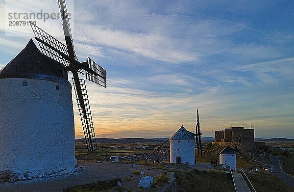 Windmills at sunset next to a castle silhouetted against a colourful sky. Atmosphere of tranquillity at dusk  aerial view  Consuegra  Toledo  Castilla-La Mancha  Spain  Europe