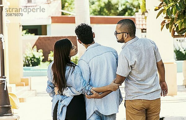 Woman holding hands with another man while walking with her boyfriend on the street. Love triangle concept. Unfaithful girl walking outdoor with her boyfriend while holding another mans hand