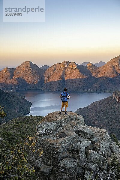 Young man standing on rocks and enjoying the view  Sunset at Blyde River Canyon View of canyon with Blyde River and table mountains in the evening light  Canyon landscape  Panorama Route  Mpumalanga  South Africa  Africa