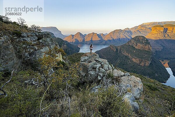 Young woman standing on rocks and enjoying the view  sunset at Blyde River Canyon with Three Rondawels peak  view of canyon with Blyde River and table mountains in the evening light  canyon landscape  Panorama Route  Mpumalanga  South Africa  Africa