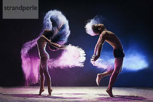 Young man and woman posing emotionally in jump in cloud of pink and blue dust studio shot