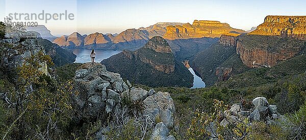 Young woman standing on rocks and enjoying the view  sunset at Blyde River Canyon with Three Rondawels peak  view of canyon with Blyde River and table mountains in the evening light  canyon landscape  Panorama Route  Mpumalanga  South Africa  Africa