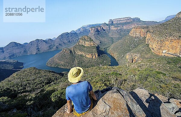 Young man sitting on a rock and enjoying the view  View of river bend at Blyde River Canyon with Three Rondawels peak  View of canyon with Blyde River and Table Mountains in the evening light  Canyon landscape  Panorama Route  Mpumalanga  South Africa  Africa