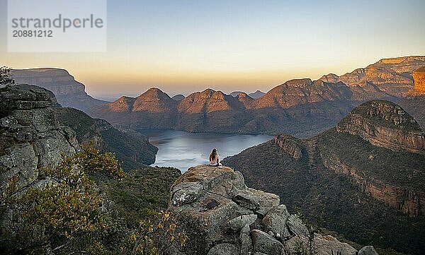 Young woman sitting on a rock  enjoying the view  sunset at Blyde River Canyon  view of canyon with Blyde River and table mountains in the evening light  canyon landscape  Panorama Route  Mpumalanga  South Africa  Africa