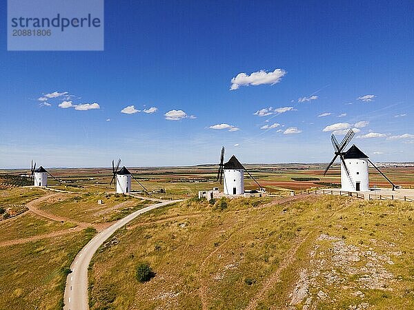 Several white windmills stand along a dirt road under a clear blue sky  aerial view  Alcazar de San Juan  Ciudad Real  Castilla-La Mancha  Route of Don Quixote  Spain  Europe