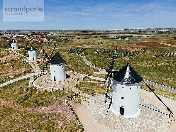 Four white windmills with black roofs on a wide hill under a clear blue sky and surrounded by fields  aerial view  Alcazar de San Juan  Ciudad Real  Castilla-La Mancha  Route of Don Quixote  Spain  Europe