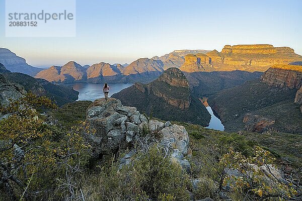 Young woman standing on rocks and enjoying the view  sunset at Blyde River Canyon with Three Rondawels peak  view of canyon with Blyde River and table mountains in the evening light  canyon landscape  Panorama Route  Mpumalanga  South Africa  Africa