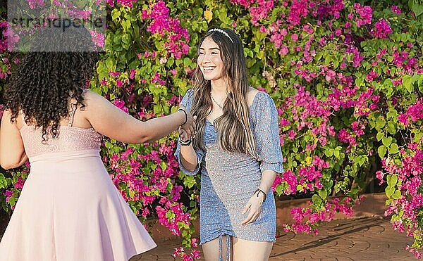 Two girls friends waving and shaking hands outdoors. Two smiling girls shaking hands on the street