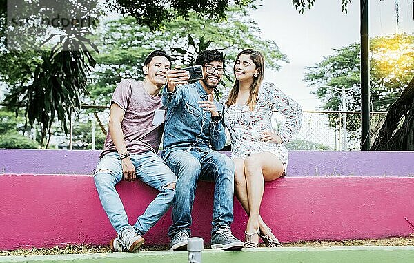 Lifestyle of three friends sitting in a park taking a selfie  Three teenage friends sitting in a park taking selfies. Meeting of three happy friends taking a selfie sitting in the park