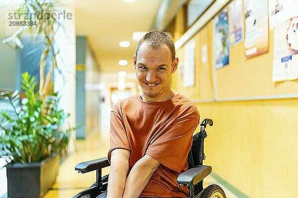 Man with disability sitting in wheelchair smiling at camera in the corridor of coworking