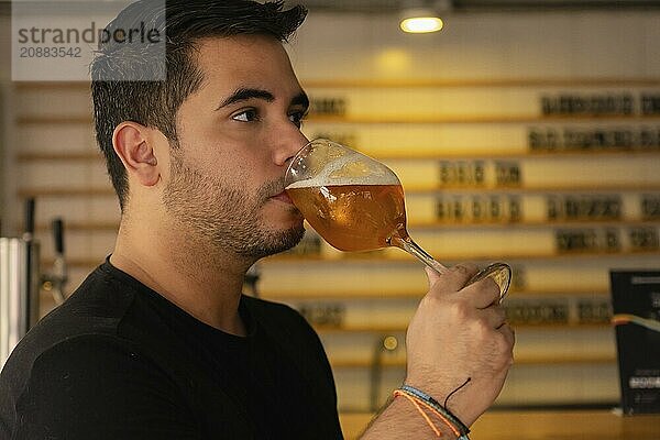 Close-up of a young Latino enjoying a glass of beer in a pub. His satisfied expression and relaxed attitude highlight the social and informal atmosphere of the place  emphasizing the pleasure of savoring a refreshing drink