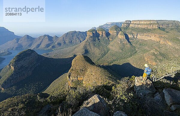 Tourist standing on a rock and enjoying the view of the canyon  Blyde River Canyon with Three Rondawels peak  View of canyon with Blyde River and Table Mountains  Canyon landscape in the evening light  Three Rondavels Viewpoint  Panorama Route  Mpumalanga  South Africa  Africa