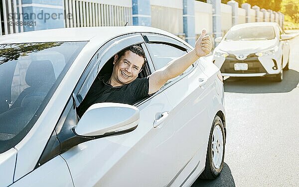 Smiling driver giving a thumbs up on the road. Satisfied driver man showing thumb up  safe driving concept. Young driver man in the car showing thumb up