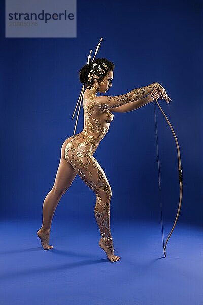 Full length of sensual confident female model with shine golden paint on naked body and elf ears