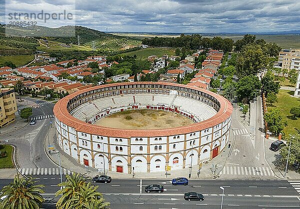 Aerial view of a historic bullring with red roofs in the middle of a city  surrounded by green trees and streets under a cloudy sky  aerial view  bullring  Cáceres  Caceres  Caçris  Extremadura  Spain  Europe